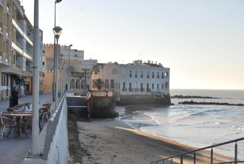 a beach with buildings and tables and the ocean at Hostal Avenida by Bossh! Hotels in Chipiona