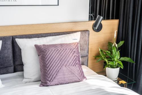 a bed with a purple pillow and a plant at Apartamenty Fenomen - Premium Porto, Nadmorskie Tarasy FREE PARKING, SWIMMING POOL, SAUNA AND OTHER! in Kołobrzeg