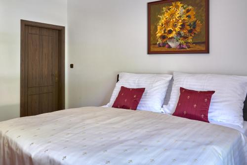 a white bed with red pillows and a painting on the wall at Vila Lovců králových in Český Krumlov