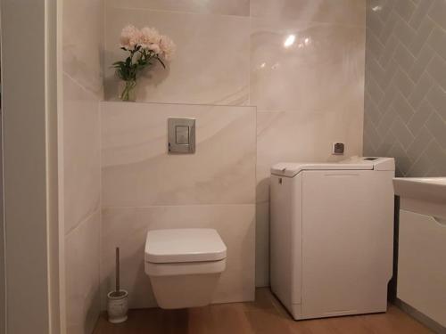 a white bathroom with a toilet and a vase of flowers at Mazowiecka Park in Kołobrzeg