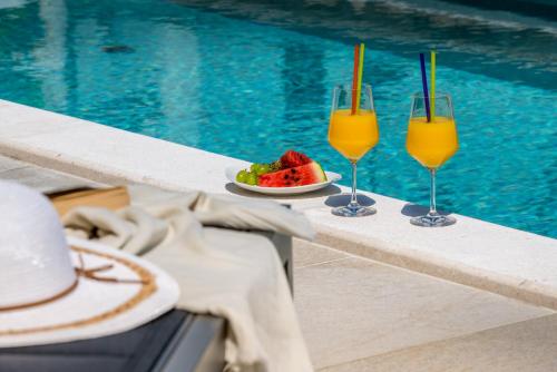 two glasses of orange juice and a plate of fruit next to a pool at Apartments Aldo in Cavtat