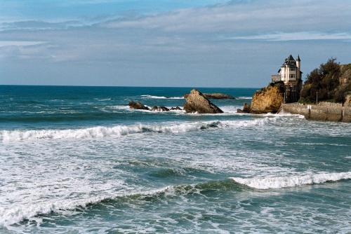 une maison sur des rochers dans l'océan avec des vagues dans l'établissement Carlina Lodge, à Biarritz