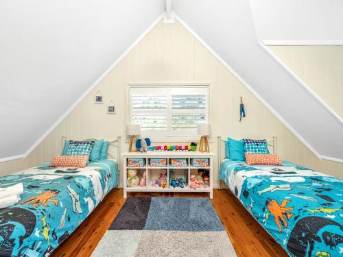 a attic bedroom with two beds and a book shelf at Mermaid Cottage at Hyams Beach in Hyams Beach