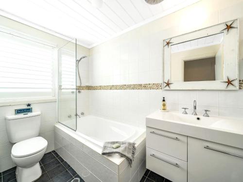 a white bathroom with a toilet and a sink at Mermaid Cottage at Hyams Beach in Hyams Beach
