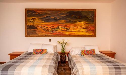 two beds in a room with a painting on the wall at Villas de Santa Ana in Manuel F. Martínez