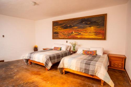 two beds in a room with a painting on the wall at Villas de Santa Ana in Manuel F. Martínez