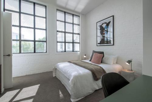 a white bedroom with a bed and two windows at Apartments on Moray in Dunedin