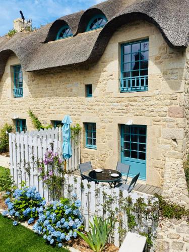 une maison en pierre avec une clôture blanche et des fleurs dans l'établissement Chaumière des Dunes à 350m de la plage de Kerhillio, à Erdeven