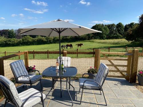 a table and chairs with an umbrella and horses in a field at Glebe Barn, Little Glebe Farm in Cheltenham