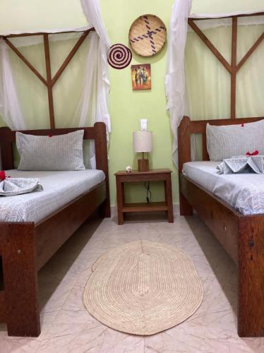 a room with two beds and a table with a lamp at Highland Bungalows in Nungwi