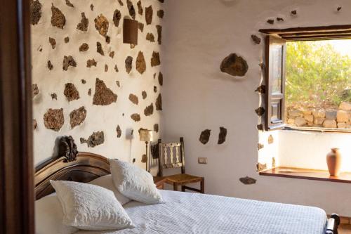 1 dormitorio con 1 cama y una ventana con rocas en la pared en Joya del Jable, en Tao