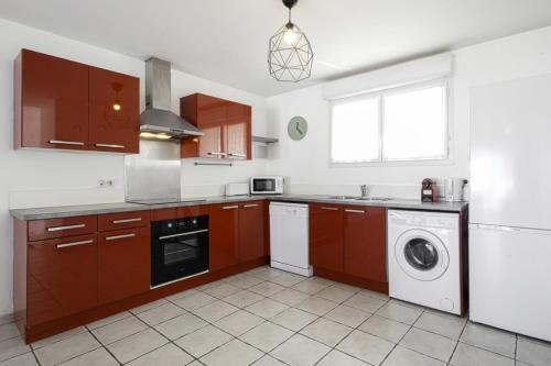 une cuisine avec des placards bruns et un lave-linge/sèche-linge dans l'établissement Triplex Laharie - Welkeys, à Bayonne