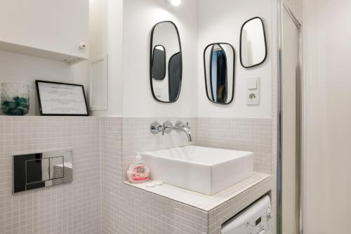 La salle de bains est pourvue d'un lavabo et de miroirs sur le mur. dans l'établissement Cozy studio 10 min from Eiffel Tower Invalides Beaugrenelle, à Paris