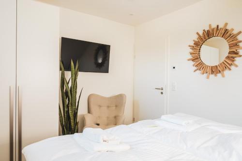 ein Schlafzimmer mit einem Bett mit einem Spiegel und einem Stuhl in der Unterkunft Dünenquartier Apartment 22 in Zingst