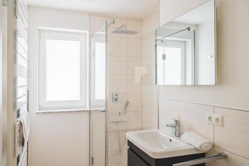 ein weißes Bad mit einem Waschbecken und einer Dusche in der Unterkunft Dünenquartier Apartment 22 in Zingst