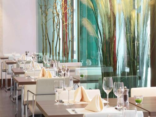 a restaurant with white tables and chairs and trees on the wall at Ibis Styles Linz in Linz