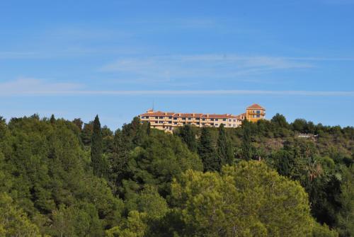 a building on top of a hill with trees at Hotel Golf Campoamor in Dehesa de Campoamor