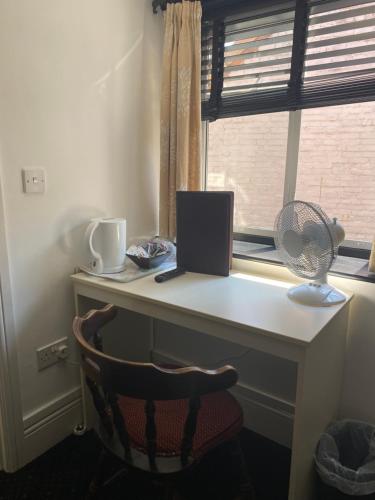 a desk with a laptop and a fan and a window at The Tudor Hotel in Bridgwater