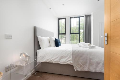 a bedroom with a bed with white sheets and a window at Modern Kingston Home close to Hampton Court Palace by UndertheDoormat in London