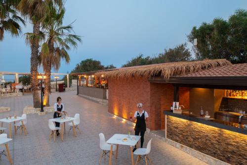 two women standing in front of a restaurant with tables and chairs at Hotel Club Eloro in Noto Marina