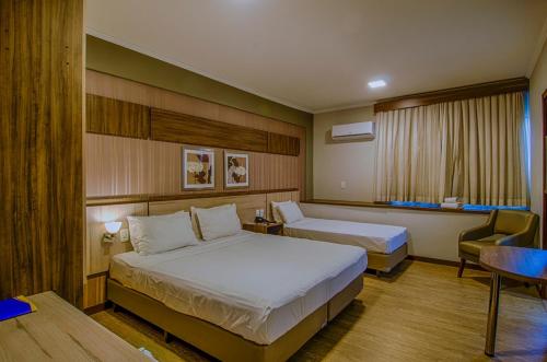 a hotel room with two beds and a chair at Klein Ville São Leopoldo in São Leopoldo