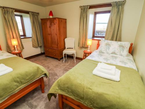 a bedroom with two beds and a chair and two windows at 1 Netherbeck Barn in Carnforth