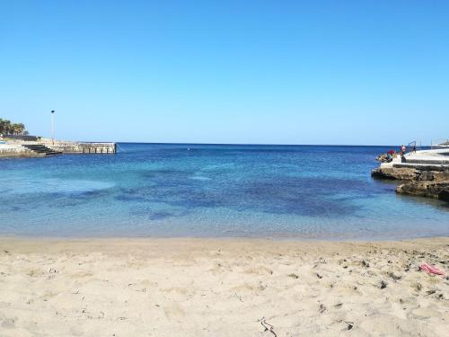 a beach with blue water and a pier at Casa Vacanze Libeccio - Villetta con giardino e piscina condominiale in Custonaci