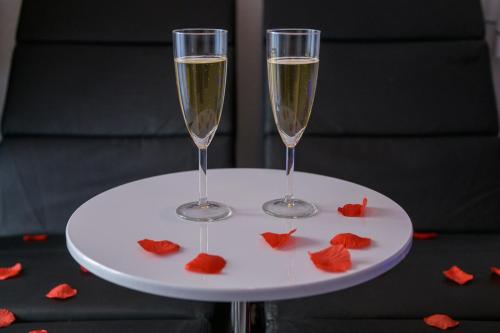 2 verres à champagne sur une table blanche avec des fleurs rouges dans l'établissement Love Room - Suite romantique avec spa privatif, au Puy-en-Velay