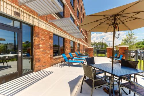a patio with blue tables and chairs and an umbrella at Holiday Inn Express - Wilmington - Porters Neck by IHG in Wilmington