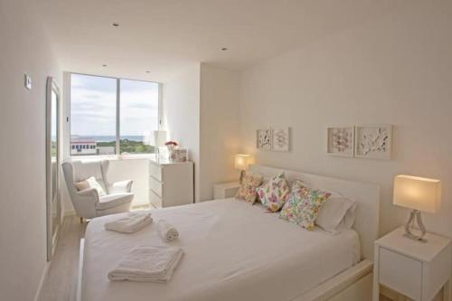 a white bedroom with a large white bed and a window at Magnificent 1 Bedroom Apartment With Views Over The Ocean in Costa da Caparica