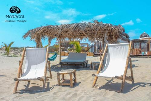 two chairs on the beach with a straw hut at Maracol Bungalows Vichayito in Vichayito