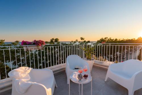 een balkon met witte stoelen en een tafel met wijnglazen bij Sunset Terrace Mazara in Mazara del Vallo