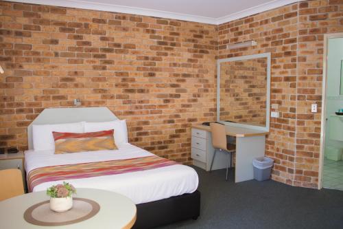 a bedroom with a bed and a brick wall at Golf Club Motor Inn Wingham in Wingham