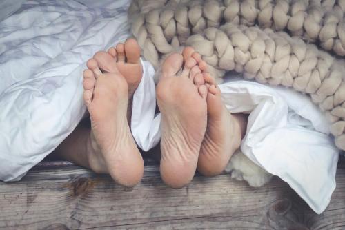 a person laying in bed with their feet on a blanket at Karkausmäen Kammari in Kinnula