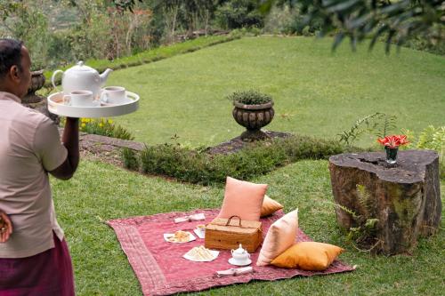 a woman holding a plate of tea on a picnic blanket at Jetwing Warwick Gardens, A Luxury Reserve in Nuwara Eliya