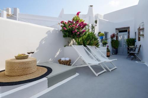 a patio with white chairs and flowers on a wall at Betty's Home Santorini in Karterados