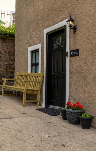 a wooden bench sitting outside of a door with flowers at The Old Paint Shop Apartment - Centrally Situated in Anstruther