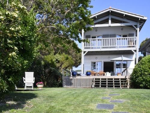 a white house with a porch and a chair in a yard at Villa De La Plage in Pyla-sur-Mer