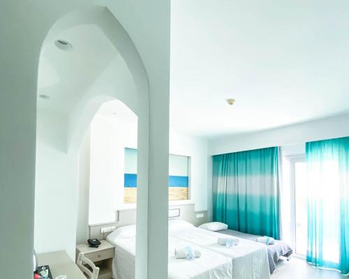 a white bedroom with two beds and a window at Anesis Hotel in Ayia Napa