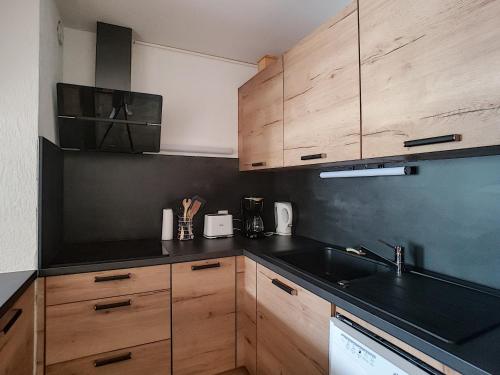 une cuisine avec des armoires en bois et un comptoir noir dans l'établissement APPARTEMENT DUPLEX SPACIEUX - SAINT JEAN D'AULPS STATION - PIED DES PISTES - 9 Personnes - RELAIS D13, à Saint-Jean-dʼAulps