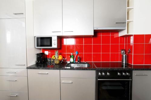 a kitchen with white cabinets and a red tile wall at HITrental Oerlikon Apartments in Zürich