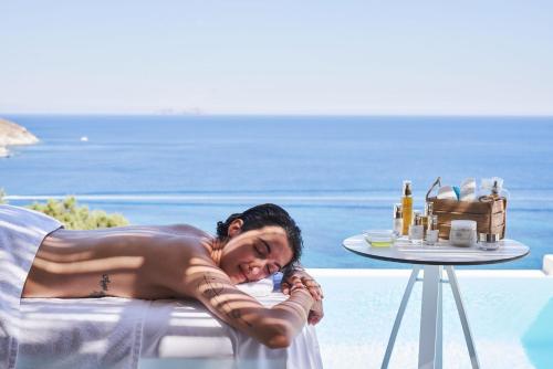 a woman laying on a chair next to a table at Radisson Blu Euphoria Resort, Mykonos in Kalo Livadi