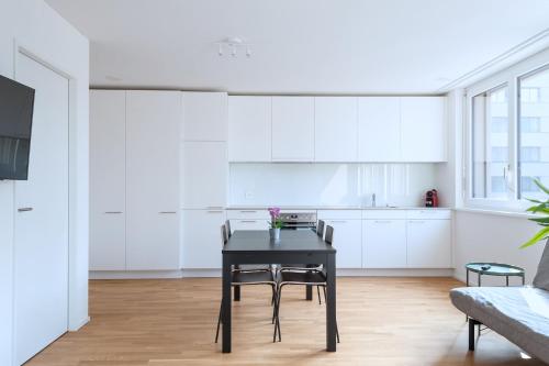a white kitchen with a black table and chairs at HITrental Messe Apartments in Basel