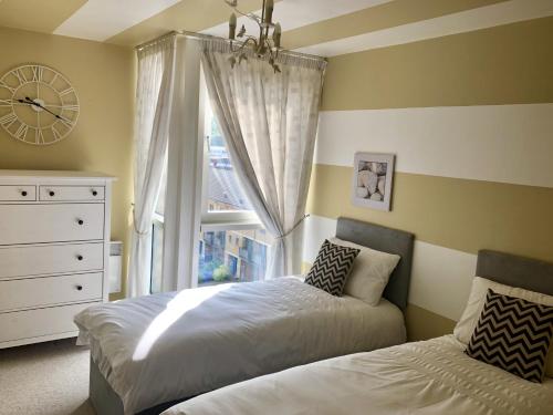 a bedroom with two beds and a window with a clock at Toothbrush Apartments - Ipswich Waterfront - Anchor St in Ipswich