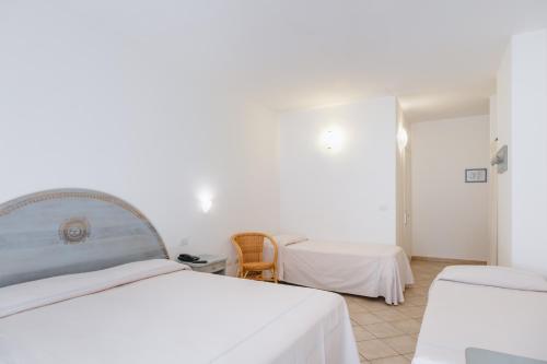 a white bedroom with two beds and a table at Hotel Angedras in Alghero