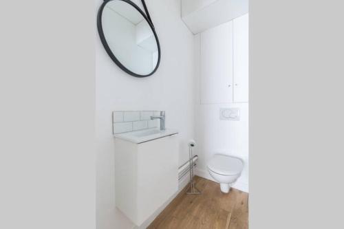 La salle de bains blanche est pourvue d'un miroir et de toilettes. dans l'établissement Appartement Duplex de Charme proche de l'opéra Garnier, à Paris