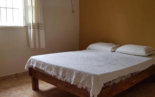 ein Bett mit weißer Bettwäsche und Kissen in einem Schlafzimmer in der Unterkunft Casa com churrasqueira no Centro de Caraguatatuba in Caraguatatuba