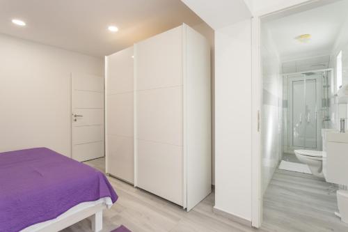 a white bedroom with a purple bed and a bathroom at Apartment Danica in Poličnik
