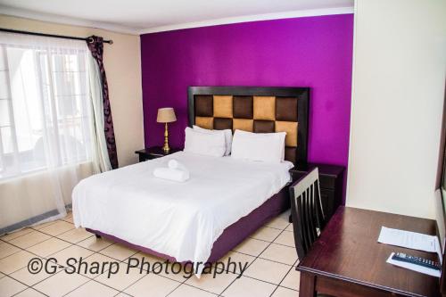 - une chambre avec un grand lit et un mur pourpre dans l'établissement @431 Rupert Street, à Pretoria