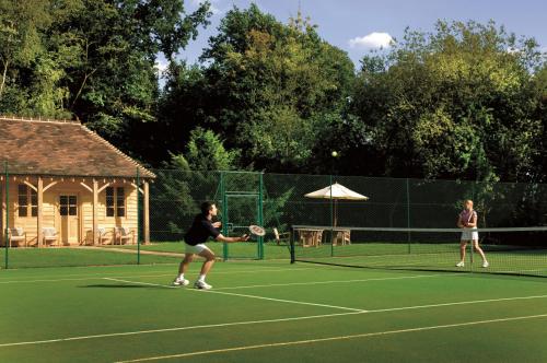 two women playing tennis on a tennis court at Four Seasons Hotel Hampshire in Winchfield